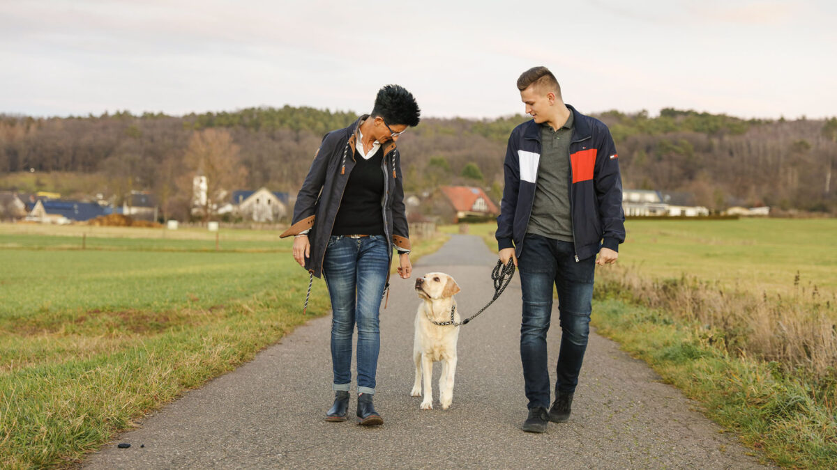 Eine Frau und ein junger Mann gehen Gassi und schauen auf ihren Hund herunter.