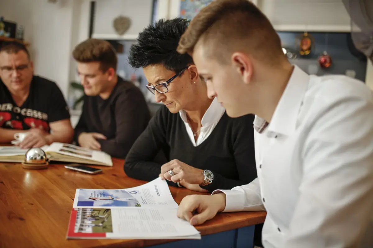 Drei Männer und eine Frau sitzten an einem Tisch und studieren ein Fotoalbum und einen Prospekt.