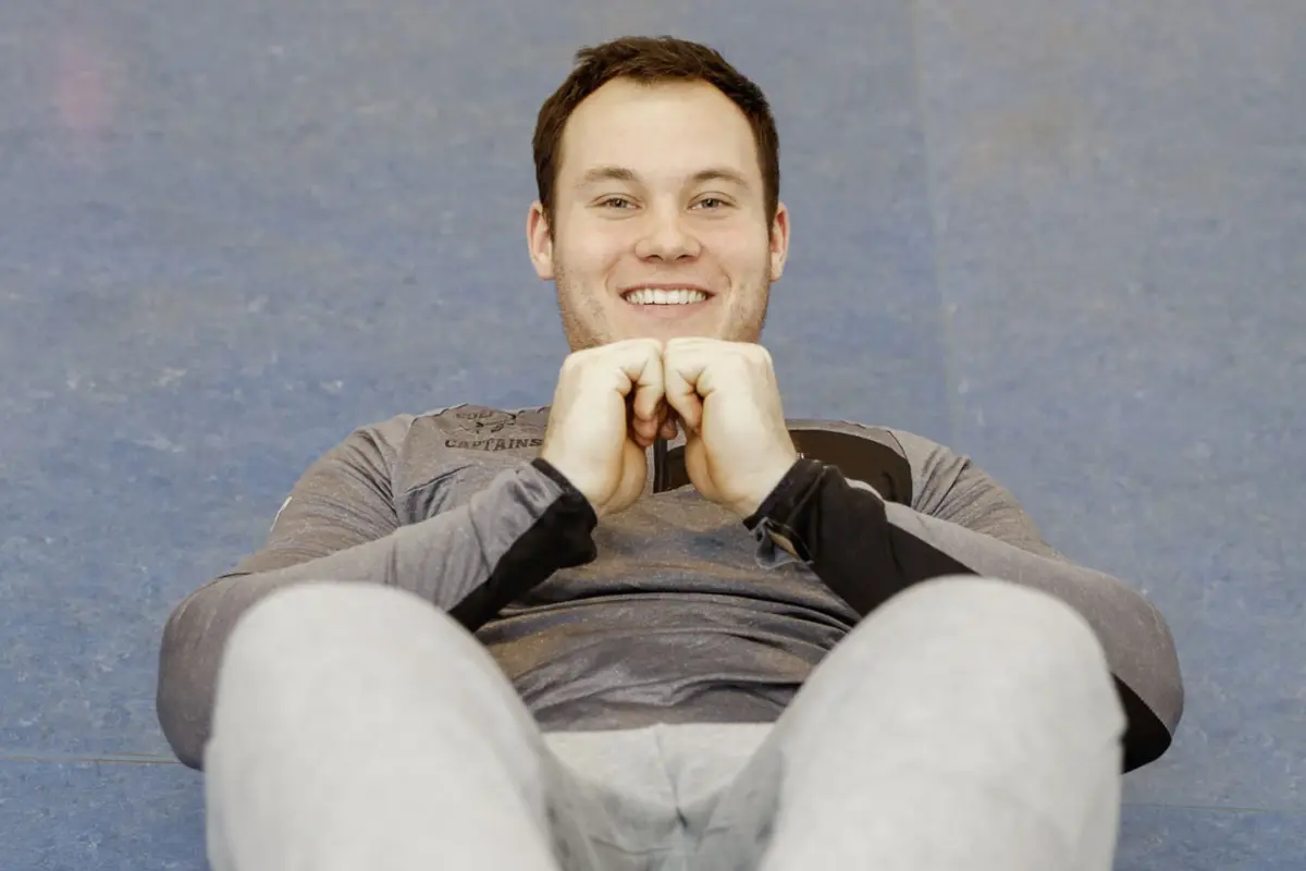 Ein junger Mann blick in die Kamera und macht gerade Sit-Ups.