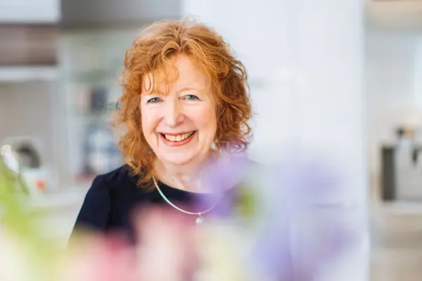 Eine Dame mit roten Haaren blickt lächelnd in die Kamera.