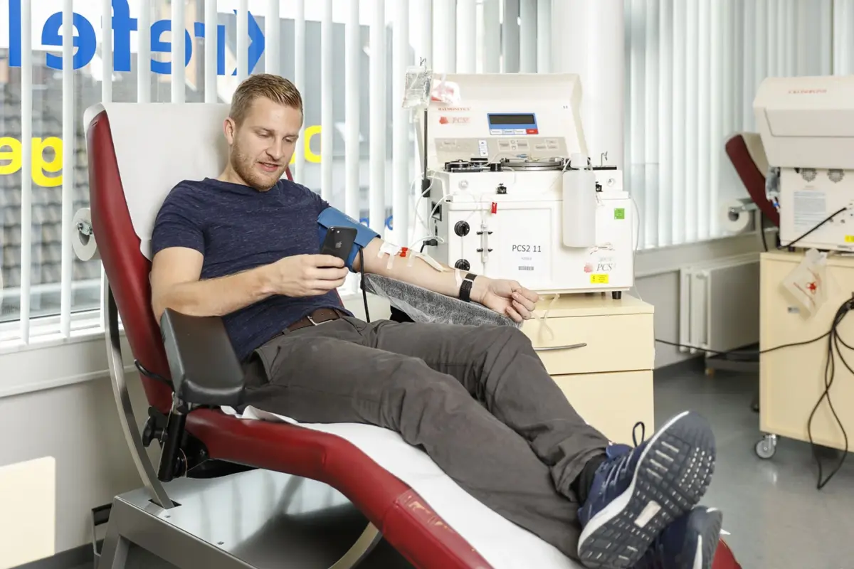 Ein Mann blickt auf sein Handy und spendet Plasma.