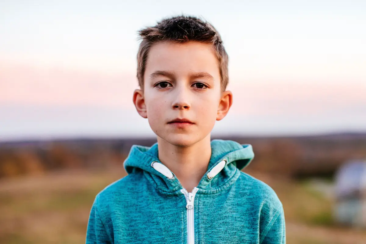 Ein Junge mit einem blauen Pullover blickt ernst in die Kamera.