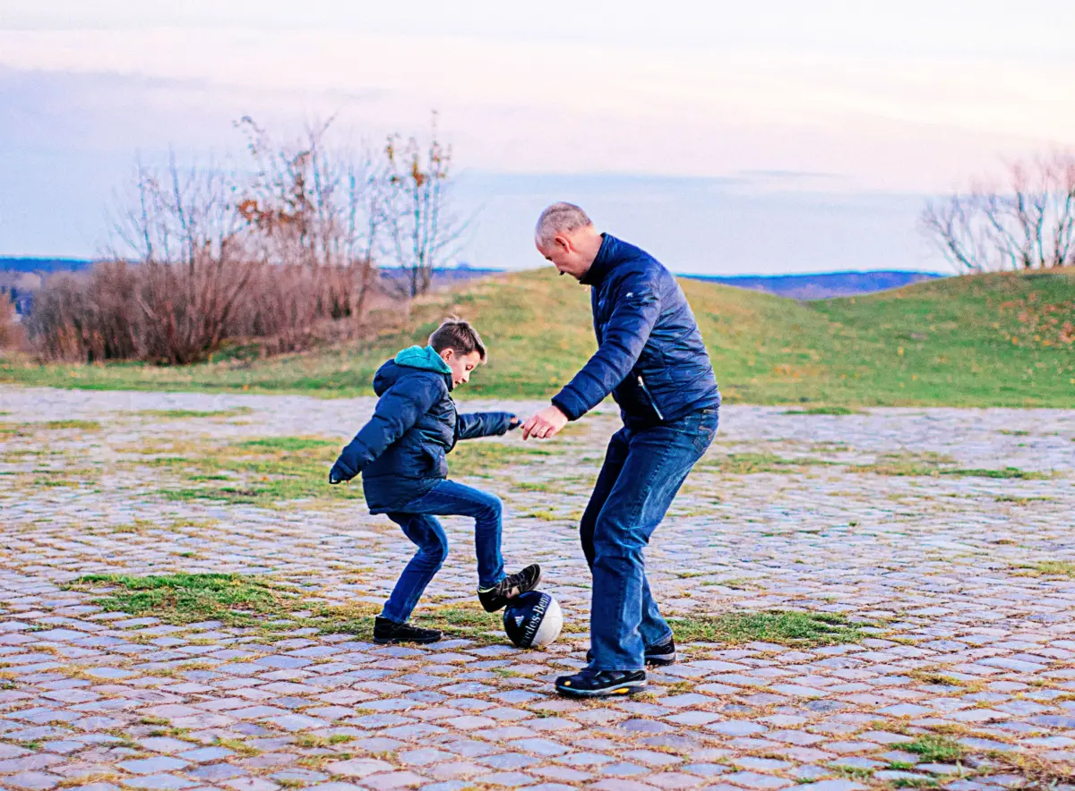 Ein Junge spielt mit einem Mann Fußball auf einem gepflasterten Platz.