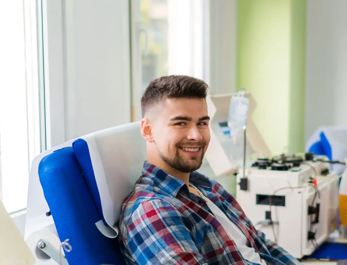 Ein junger Mann spendet Blut und befindet sich in einem Spendesaal. Dabei wird es von einer medizinischen Mitarbeiterin betreut.
